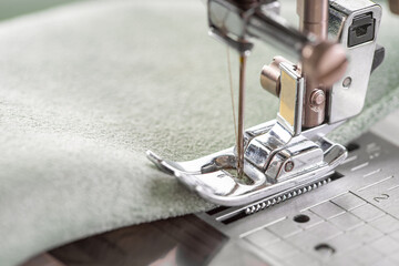 Modern sewing machine presser foot with green fabric and thread, closeup, macro. Sewing process...