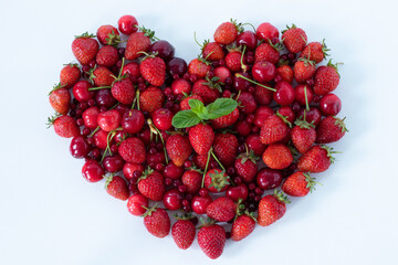 Strawberries and cherries in a heart shape isolated on white. Top table view. A close-up. Fresh...