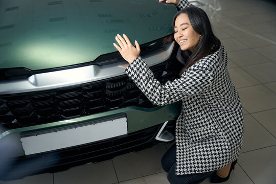 Happy beautiful woman hugging a shining car hood