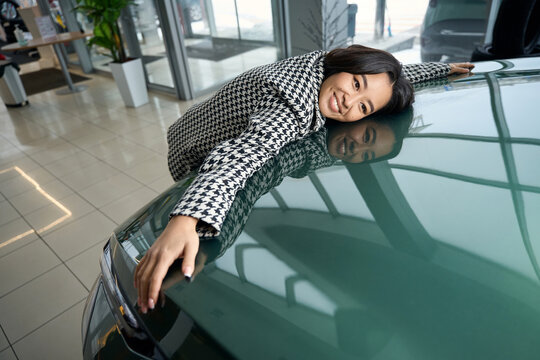 Happy young asian woman hugging the hood of new car