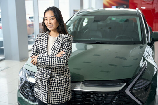 Beautiful brunette stands against the backdrop of sparkling new car