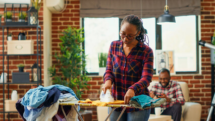 Frustrated housewife getting tired and angry about doing chores by herself, ironing laundry with steam and heat in apartment. Young adult being unhappy and stressed about housework.