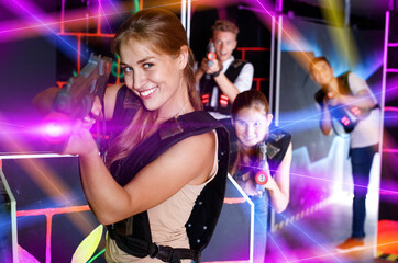 Portrait of exciting glad girl with laser pistol playing laser tag in dark room