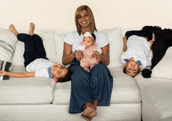 Beautiful African American woman sitting on couch with baby girl on her lap; her six year old twin boys sprawling in playful upside down poses next to them