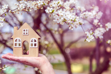 The girl holds the house symbol against the background of blossoming cherry
