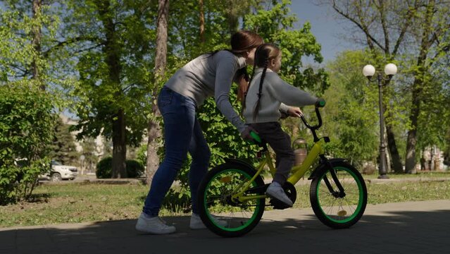 happy family moments, playful girl, little daughter learns ride two-wheeled bicycle for first time, cardio, mom little daughter learn ride bike nature, child pedals wheels, happy family in the park