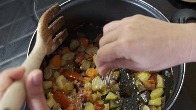 hand stirring a vegetable stew or stir-fry with a wooden spoon, close-up image of the preparation of a traditional homemade dish
