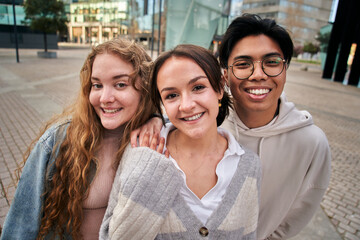 Portrait of three smiling multiracial young college students. Happy friends hugging pose nice...