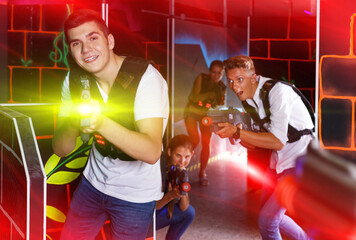 Fototapeta na wymiar smiling young men and women playing emotionally laser tag game in arena