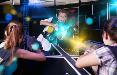 Excited adult people playing enthusiastically laser tag game two teams opposite each other in dark...