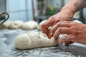 Selective focus of a baker's hands kneading wholemeal bread on a steel table