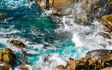 Surfer waves turquoise blue water rocks cliffs boulders Puerto Escondido.