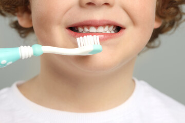 Cute little boy brushing his teeth with plastic toothbrush on light grey background, closeup