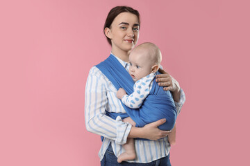 Mother holding her child in sling (baby carrier) on pink background