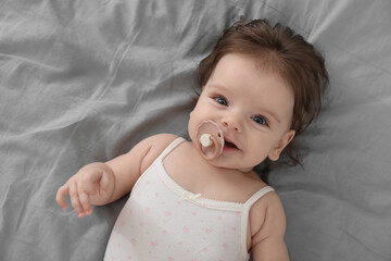 Cute little baby with pacifier on bed, top view