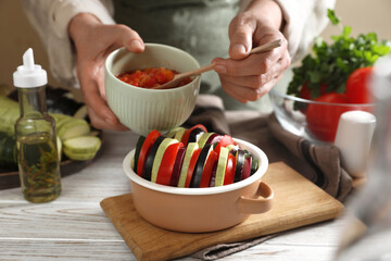 Cooking delicious ratatouille. Woman dressing fresh vegetables in bowl at white wooden table, closeup