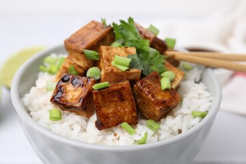 Bowl of rice with fried tofu and greens on white table, closeup