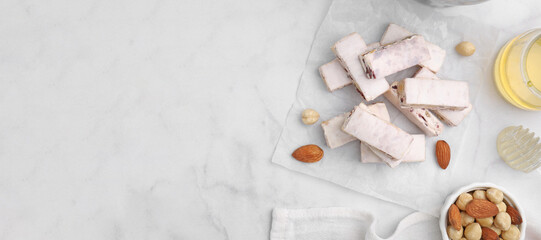 Fototapeta na wymiar Pieces of delicious nutty nougat and ingredients on white marble table, flat lay. Banner design with space for text