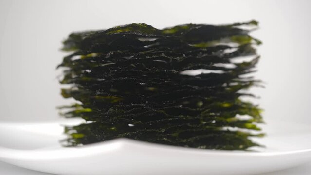 crispy dried nori seaweed rotates in a white plate on a white background. side view. healthy snack, the concept of oriental cuisine.