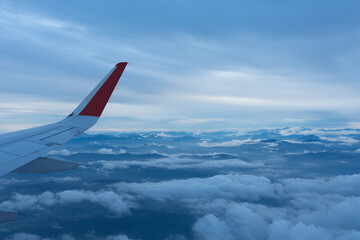 Wing of an airplane flying above mountain peaks covered with clouds. View of the hills from the airplane.