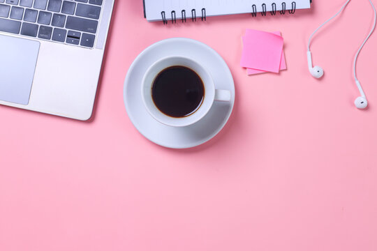 Minimalist women office desktop with laptop, cup of coffee, earphones, sticky notes and notebook on pink background. Flat lay, top view, space for text.
