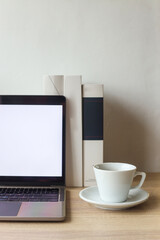 Potrait of comfortable workplace with open blank screen laptop computer, coffee cup and books on wooden desk