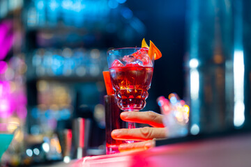 Professional male bartender preparing and serving cocktail drink to customer on bar counter at...