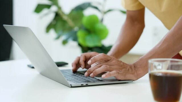 Close-up Asian man's hand typing on laptop computer lying on table there is coffee mug placed nearby, man hurriedly typed backlog boss when got message speed up deliver before time runs out.