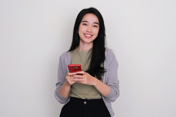 Naklejka premium Young Asian woman smiling at the camera while holding a mobile phone
