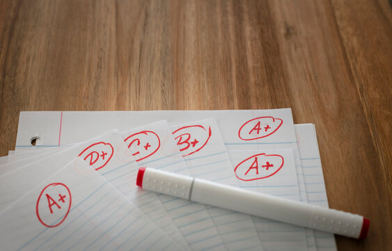 Different grades school paper marked in red ink over a wood desktop. Test results concept.