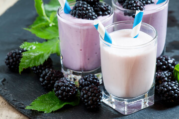 Milkshake with wild blueberries and blackberries with striped straws on a dark background,...