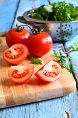Obraz na płótnie Canvas Fresh red tomatoes whole and in the context of the old painted wood surface against the green salad leaves and a metal colander