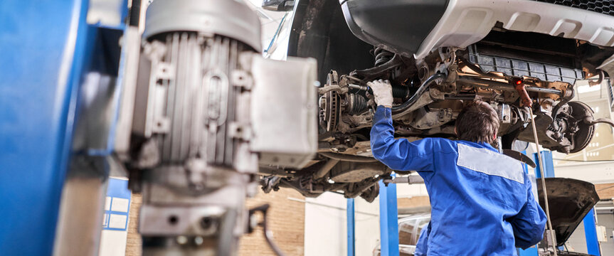Car mechanic inspecting car steering rod and repair suspension detail. Lifted automobile at repair service station. replacement of ferrule and leverage