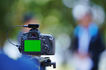 DSLR camera on tripod with green screen isolated over bokeh background.