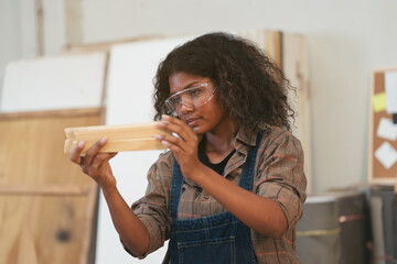Female carpenter working in wood workshop. Female joiner wearing safety uniform and working in...