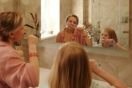Caucasian woman and her daughter standing in bathroom in front of mirror brushing teeth in morning