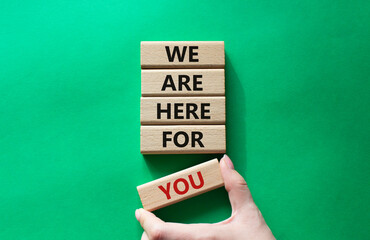 Help symbol. Wooden blocks with words We are here for you. Beautiful green background. Businessman hand. Business and We are here for you concept. Copy space.