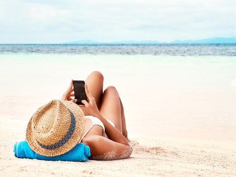 Travel, phone and woman relaxing on the beach scrolling on social media or mobile app on holiday. Rest, tropical and female person laying on sand by ocean networking on cellphone on summer vacation.
