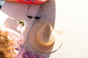 Sunhat, sunglasses and cocktail between couple sitting by swimming pool in the sun, with copy space