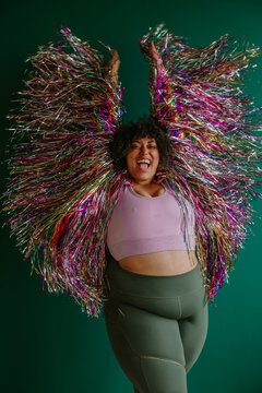 plus size black person with arms in the air wearing a rainbow tinsel jacket