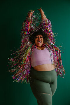 plus size black person with arms in the air wearing a rainbow tinsel jacket