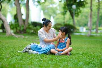 Mother and little daughter sitting on the grass together in the park. Mother having fun with her little daughter outdoors in green nature park. Happy family concept. Mother's Day