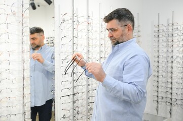 Naklejka na ściany i meble Senior man choosing glasses in optical store, try on eyeglass frames to decide on the perfect one