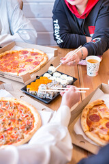 two young women are sitting at the wooden table and taking suchi with wooden japaneese chopsticks