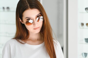 Fototapeta na wymiar A young woman chooses on sunglasses in an optics store