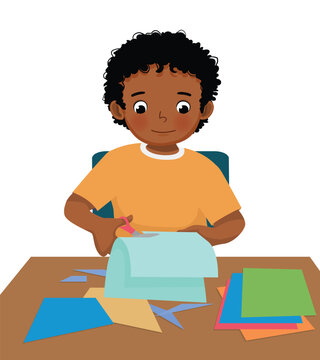 Cute little African boy cutting colored paper with scissors making heart shape paper cut art craft