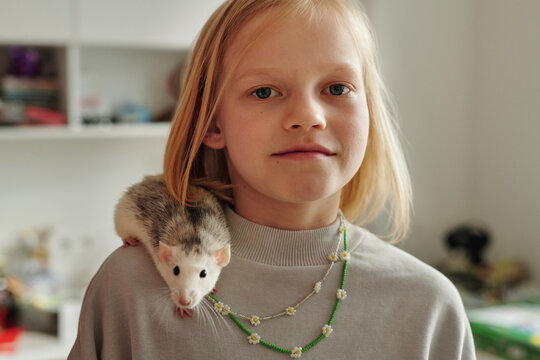 Horizontal close-up portrait of preteen Caucasian girl with blond hair and lovely pet fancy rat on her shoulder
