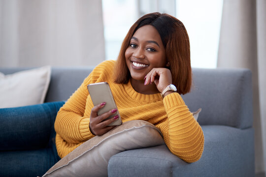 Black woman using phone, chat on social media and relax at home, smile in portrait with online communication. African female person, mobile app with text or post update with connectivity in apartment