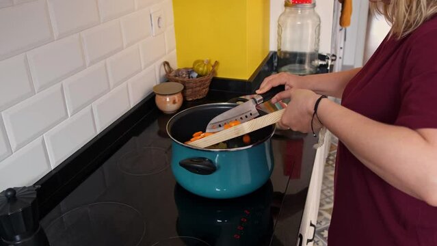 woman puts some vegetables cut into bulls into the saucepan to add them to the stew that she is preparing in the kitchen at home
