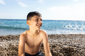A nine-year-old boy is depicted at the beach, completely soaked. His brown hair is wet, sticking to...